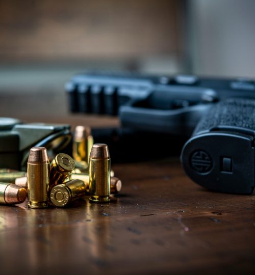 Close view of a handgun with bullets on a wooden surface, emphasizing firearms and ammunition.