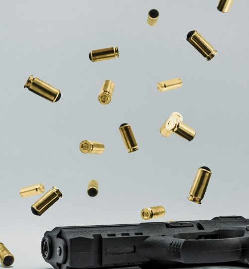Close-up of a Glock pistol with spent shell casings suspended in the air on a gray studio background.