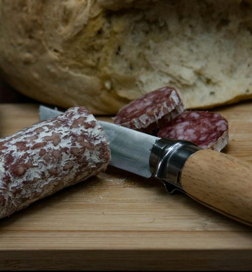 A rustic scene of fresh bread and salami on a wooden board with a knife, perfect for culinary presentations.